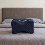 Le coussin Noctivelle bleu marine, forme sablier, matelassé, sur un lit