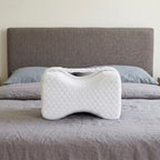 Le coussin Noctivelle blanc, forme sablier, sur un lit